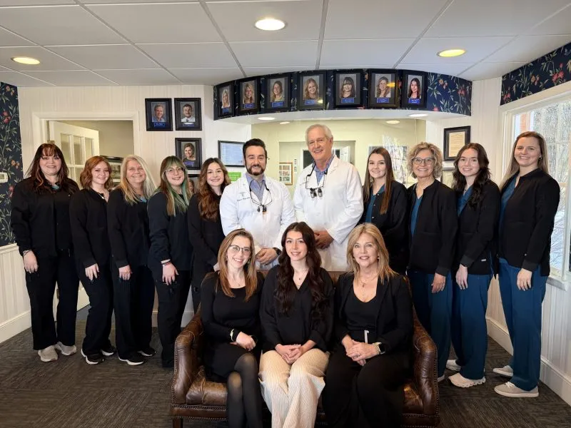 A group photo of a dental office staff, including dentists and dental assistants, posing together in their clinic.